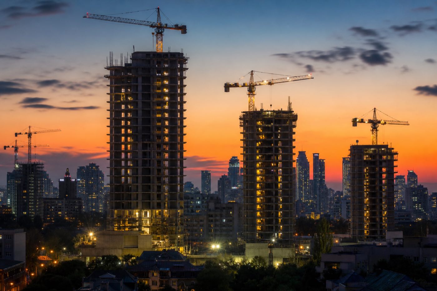 City skyline at dusk with high-rise towers and construction cranes